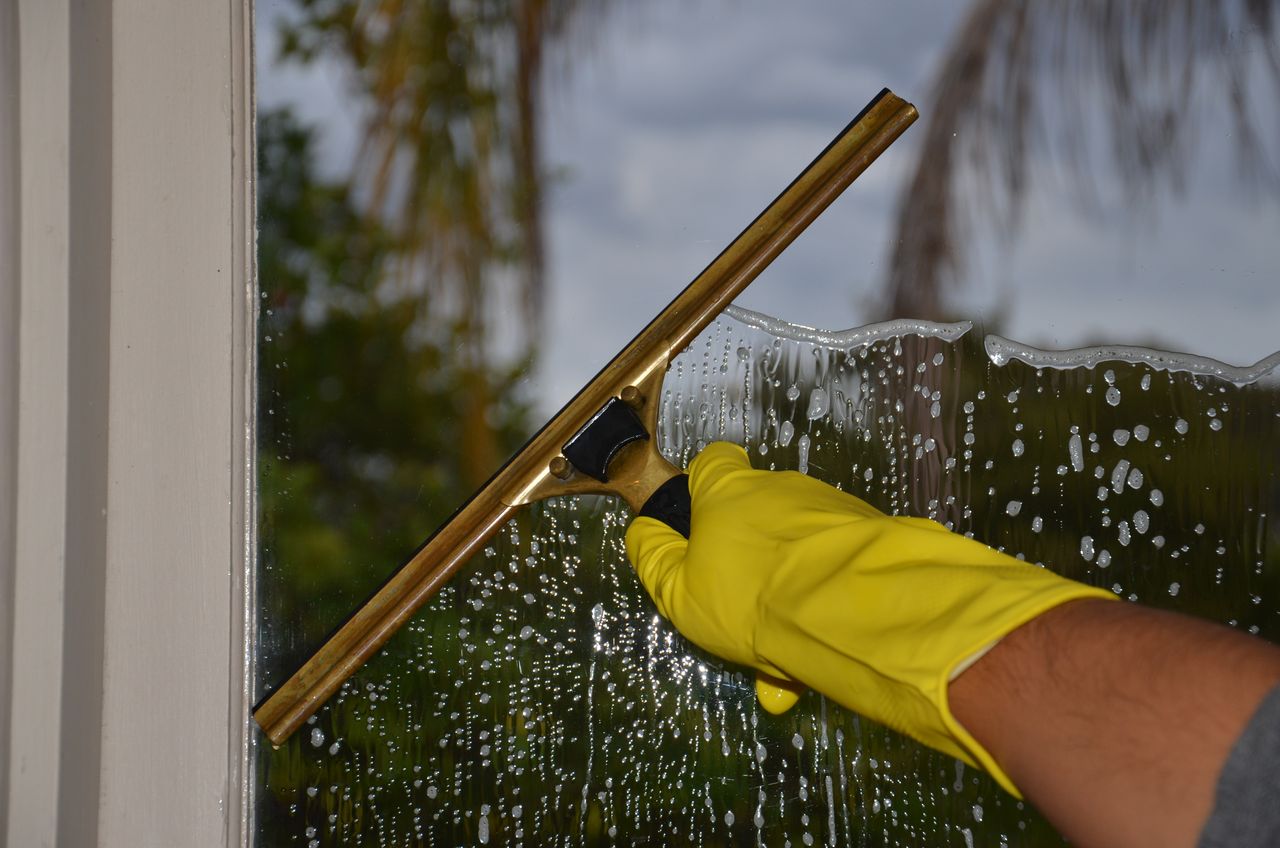 team-01 Close-up of hand cleaning window with squeegee outdoors using yellow gloves.